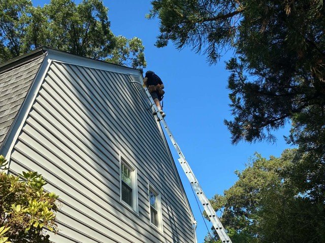 Magothy Roofing and Exteriors crew member on an extension ladder during a siding job